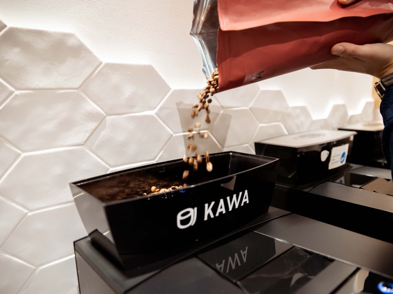Versement de grains de café torréfiés dans le bac d'une machine KAWA